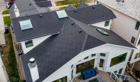 Aerial view of a modern white house with a dark gray shingled roof featuring multiple skylights.