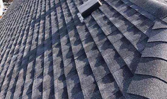 A close-up view of a gray asphalt shingle roof with a vent and textured pattern.