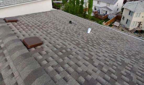 An aerial view of a residential roof covered in gray asphalt shingles with two brown vents and a white object.