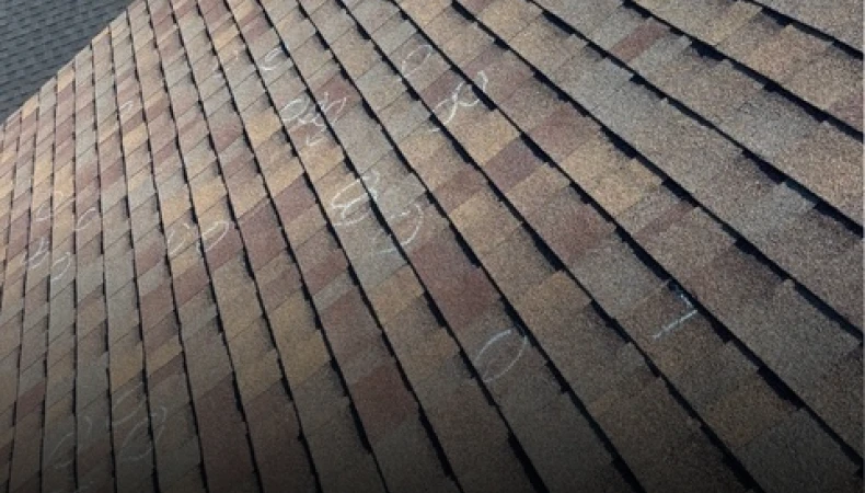 A close-up view of a roof covered in textured asphalt shingles with faint chalk markings drawn on them.