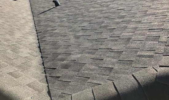 Close-up of a gray asphalt shingle roof with visible texture and shadow patterns.