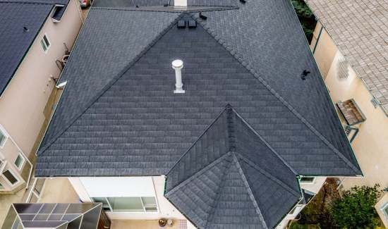 Aerial view of a house with a dark gray shingle roof featuring a chimney and multiple gables.