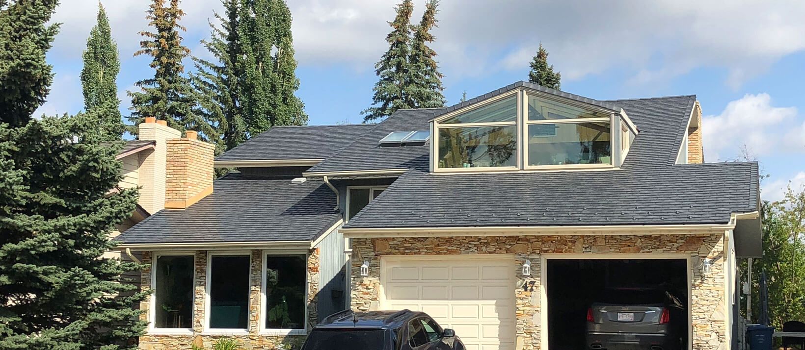 A modern two-story house with stone accents and a large glass dormer window under a dark shingle roof.